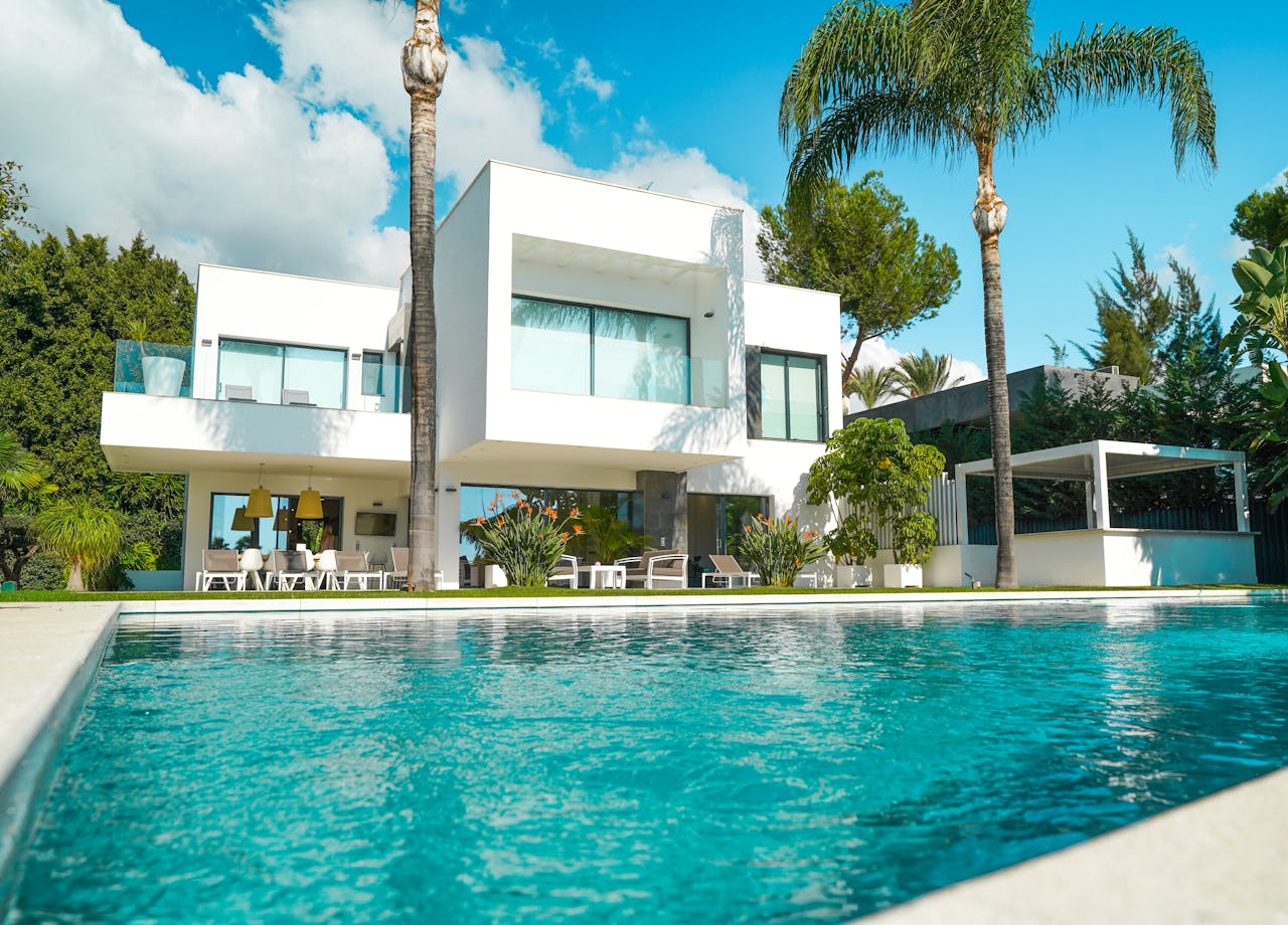about-us-01 A stunning modern luxury villa with a pool, surrounded by lush greenery and bathed in sunlight.